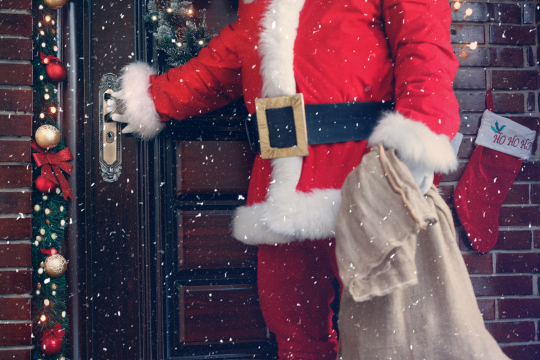 Weihnachtsmann legt Hand auf Türklinke, um anzudeuten, dass er das Haus betreten möchte