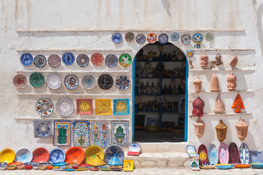 Blick auf einen Shop in einer tunesischen Altstadt mit bunt bemalter Keramik an Wänden und auf dem Boden vor dem Shop